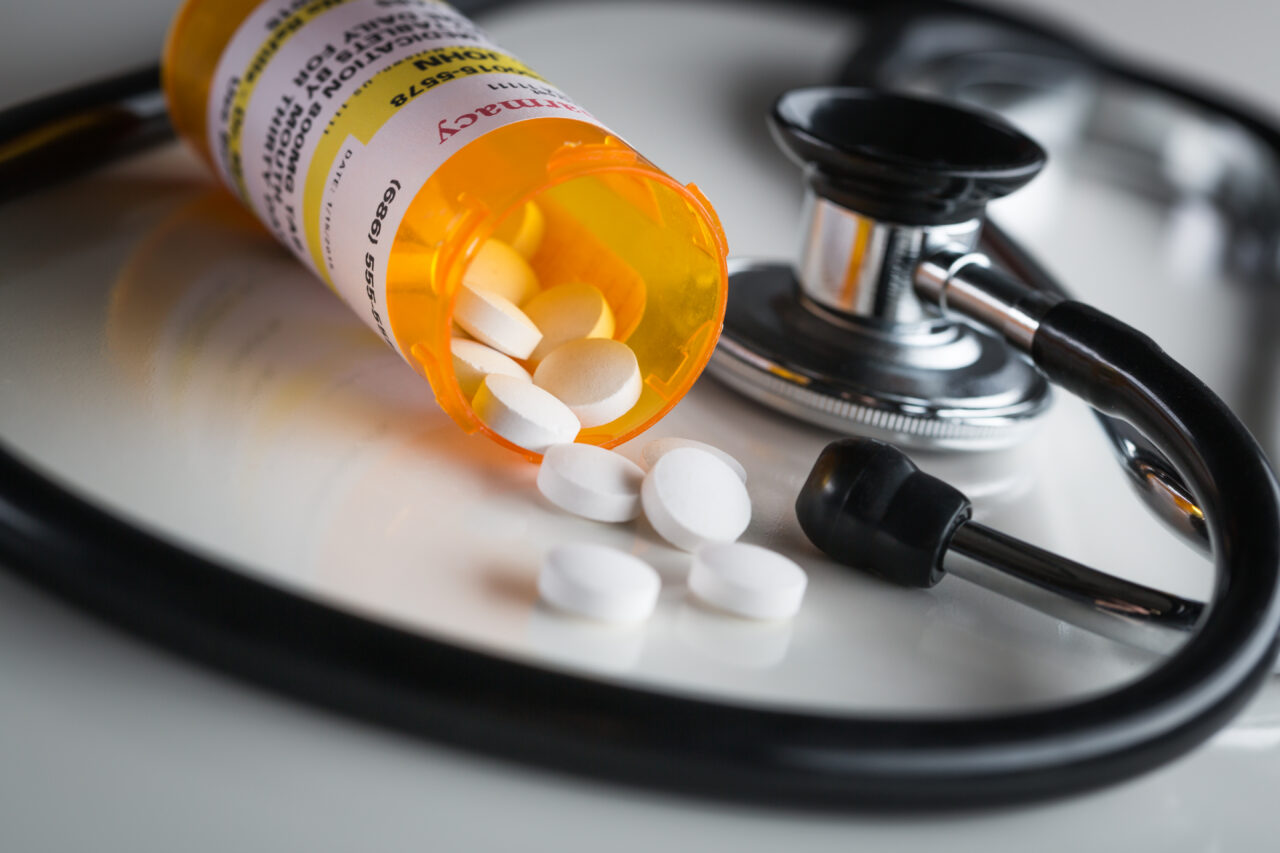 Open orange prescription bottle with white pills spilling onto a stethoscope, suggesting possible Medication and Prescription Errors.